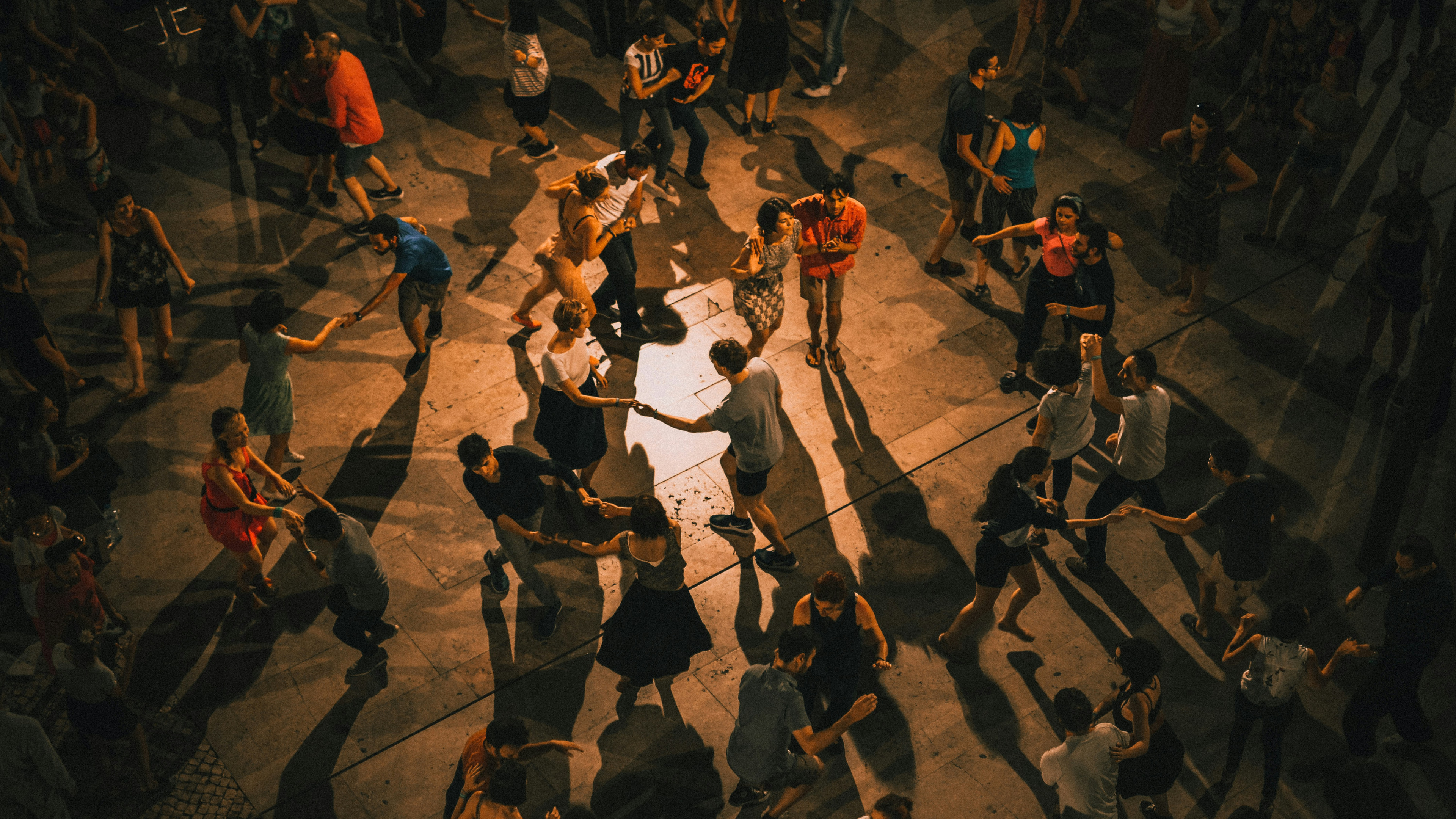 An overhead view of a packed open-air social with couples dancing under warm low light